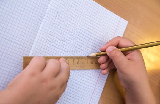 The student draws a triangle with a pencil along the ruler. A schoolboy performs a task at the workplace. The concept of children's education, teaching knowledge, skills and abilities.