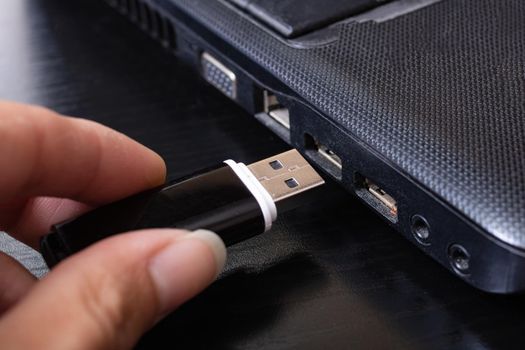 Black USB flashcard in hand and laptop close up