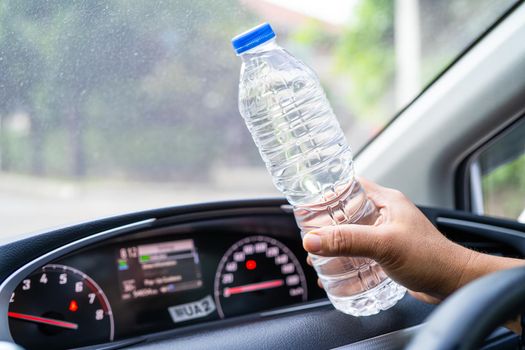 Asian woman driver holding bottle for drink water while driving a car. Plastic hot water bottle cause fire.