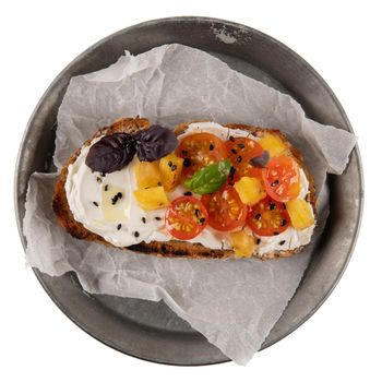 Italian bruschetta with roasted tomatoes, mozzarella cheese, pineapple slices and herbs on a metal plate isolated on white background.