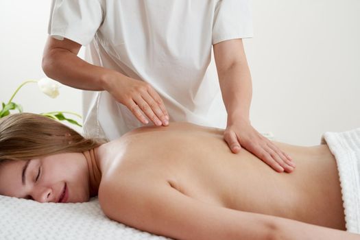 Masseur massaging young woman on massage table in a spa salon. Young woman relaxing during back massage at the spa. Spa treatment concept