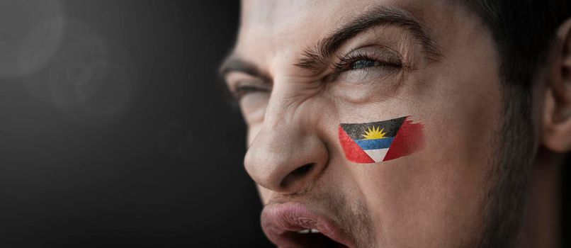 A screaming man with the image of the Antigua and Barbuda national flag on his face.