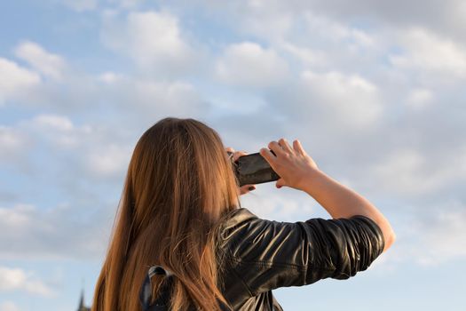 Girl tourist takes pictures of the sky with fluffy clouds on a mobile phone.