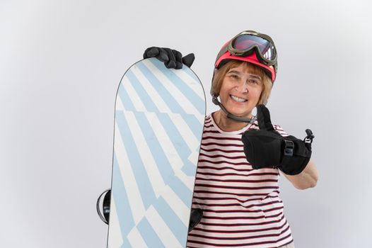 Portrait of smiling elderly woman in ski equipment showing thumb up on white background.