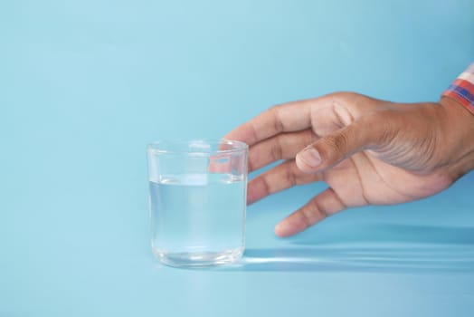 hand holding a glass of water against blue background .