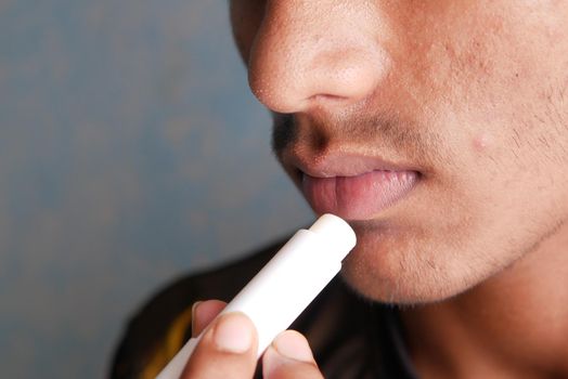 young man applying moisturising lip balm on lips.