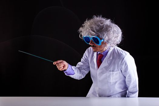 Crazy science teacher in white coat with unkempt hair in funny eye glasses holding a wand to point at the left