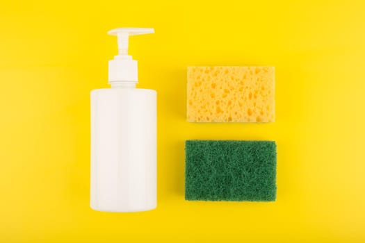 Creative minimal flat lay with detergent in white tube, and yellow and green cleaning sponges on bright yellow background. Colorful home cleaning and dishwashing concept