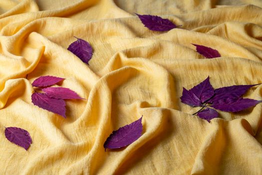 Autumn composition of red dry leaves laid out on a bright yellow crumpled cloth. Selective focus.