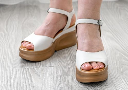 Female feet with White leather sandals stand on the floor in the room