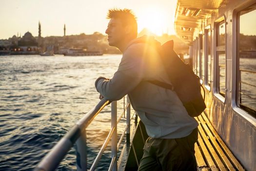 A young travelling man on a ferry floats to the shores of Istanbul, Turkey in the rays of sunset. The beginning of a great adventure.