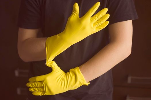 Young man puts yellow rubber gloves on his hands and plans to start cleaning the kitchen and home with disinfectant detergents.
