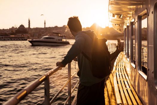 A young travelling man on a ferry floats to the shores of Istanbul, Turkey in the rays of sunset. The beginning of a great adventure.