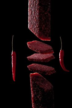 Slice of salami on black background. Flying salami and red pepper.