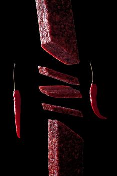 Slice of salami on black background. Flying salami and red pepper.