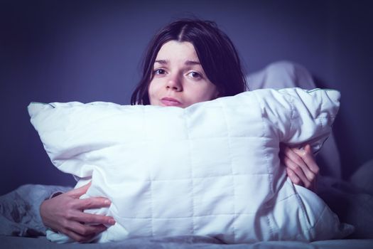 Young girl hugs a pillow and hid under a blanket from all problems, procrastinating, millennials generation. Woman covered with a blanket and is worried about insomnia, poor sleep, getting stress.