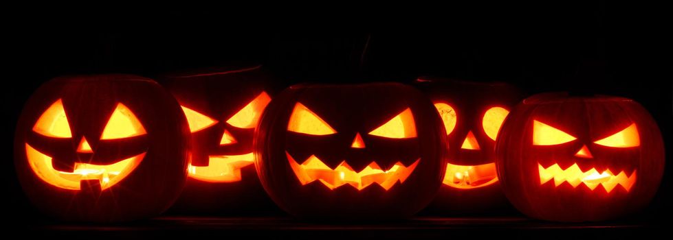 Many Halloween Pumpkin glowing faces in a row isolated on black background