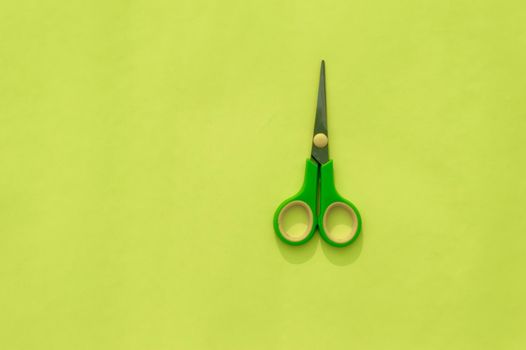 Green scissors isolated on Light green background. Table top view. Copy space for text.