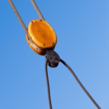 Beautiful wooden cable pulley rigging detail of traditional sail ship yacht against blue sky