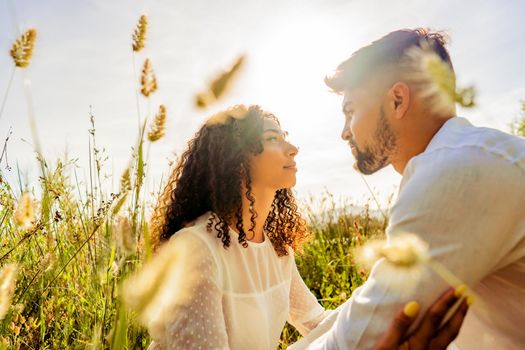 Romantic scene of multiracial passionate young couple in love looking in eyes each other among high grass vegetation at sunset or dawn with sun backlit effect Romance dream shot of lovers in nature