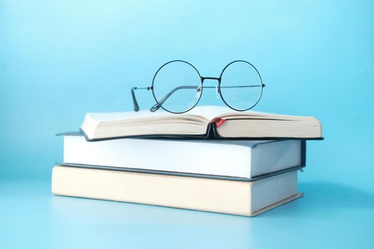 stack of books and eyeglass on blue background ,
