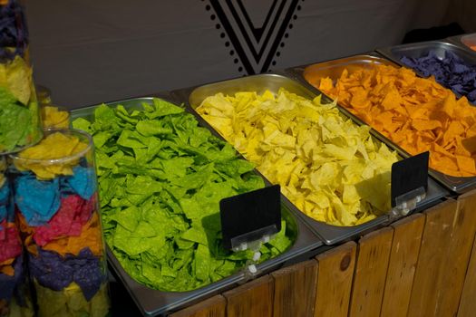 Multi colored tortilla chips in trays on the showcase. Street food festival. Selective focus.