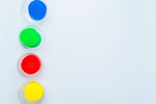 The dough for modeling red, yellow, blue and green colors is placed in a row vertically in jars on the side on a white background. High quality photo