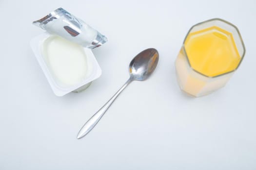 A cup of natural yogurt, a dessert spoon and a glass of orange juice on a white background. High quality photo