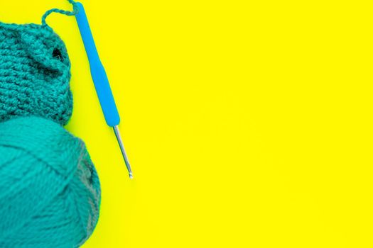 A metal hook with a blue handle, a skein of green yarn and a part of a knitted fragment lies on the side of the photo on a yellow background. top view, flat lay, copy space, isolate. High quality photo