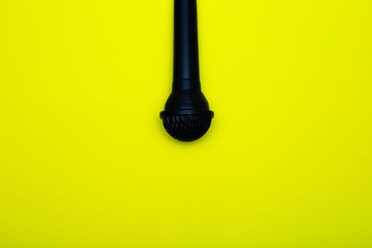 A black microphone hangs from above on a yellow background. High quality photo