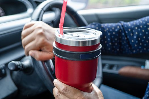 Asian lady holding ice coffee in car, dangerous and risk an accident.