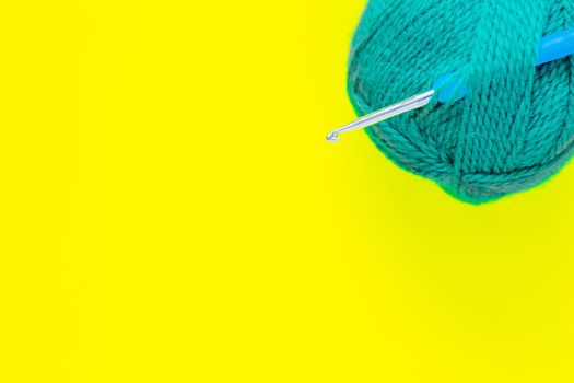 A metal hook with a blue handle is inserted into a skein of green yarn in the upper corner of the photo on a yellow background. top view, flat lay, copy space, isolate. High quality photo