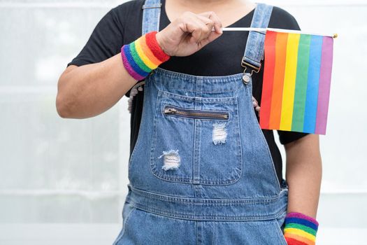 Asian lady wearing blue jean jacket or denim shirt and holding rainbow color flag, symbol of LGBT pride month celebrate annual in June social of gay, lesbian, bisexual, transgender, human rights.