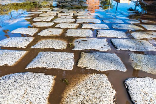 Long path full of gray stones like brick and water with reflections in puddles