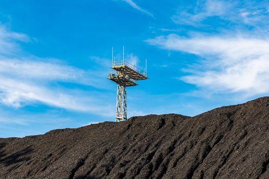 High tower with platforms and lamps on factory square behind high pile of stones and sand