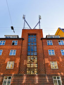 Facade of red brick building with blue reflections in windows and antennas on roof