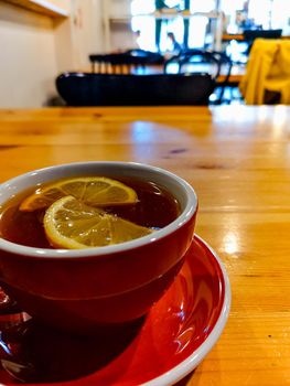 Red cup of warming tea with slice of lemon in small cafe