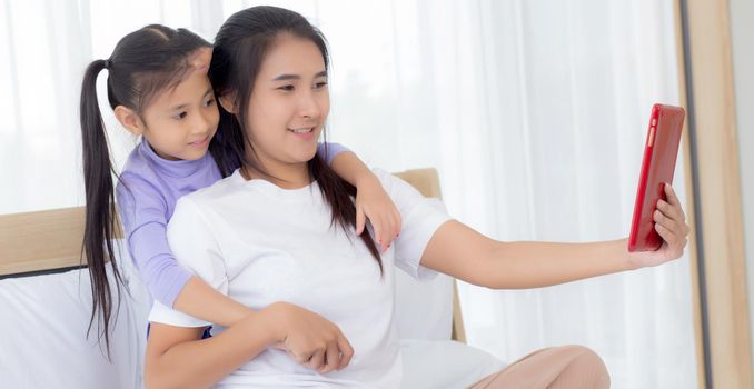 Young asian mom and daughter video call on tablet computer greeting with family together, happy mother and girl with relationship using technology in communication to internet online, two people.