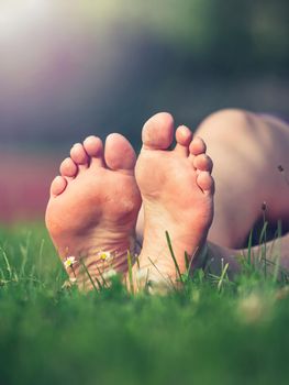 Dirty soles with hard dry skin of bare feet middle aged sporty woman. Female legs resting in fresh spring grass