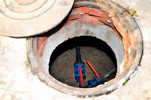 Open hatch of a concrete industrial well with communication wires inside at a construction site.