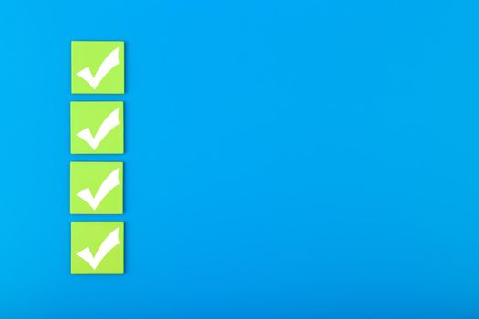 Four checkmarks on green tablets in a row on blue background with copy space. Concept of questionary, checklist, to do list, planning, business or verification. Modern minimal composition 