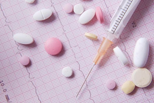 stethoscope, medical pill and syringe on a cardio diagram