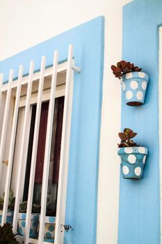 Typical Andalusian whitewashed facade with blue painted window and polka dot pots on the wall