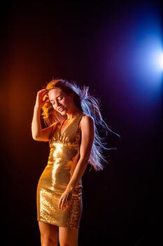 Beautiful girl in Golden dress dancing on black background, color lights