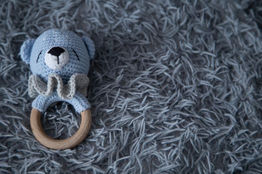 A toy for a baby in the form of a knitted bear cub lies on a fluffy gray background. High quality photo