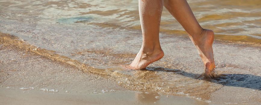 Young woman walking along the sandy beach. Female legs in the sand on the seaside