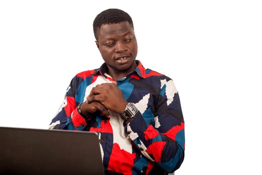 young african sitting in multicolored shirt with computer looking in profile smiling.