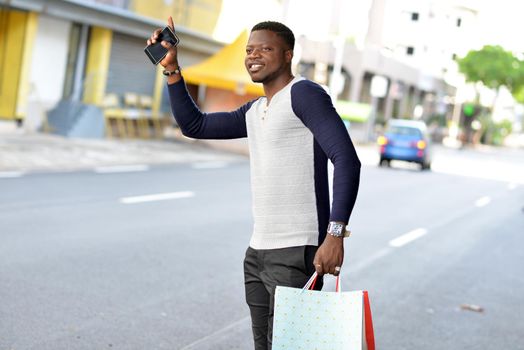 young african man standing in polo on the street after shopping and looking in front of him smiling.