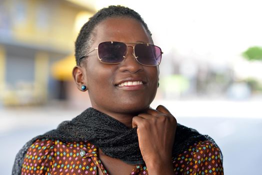 close-up of beautiful smiling woman with sunglasses and holding a black neck scarf in town.