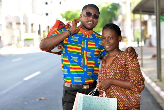 young african couple standing in shirts on the street looking in front of them smiling.